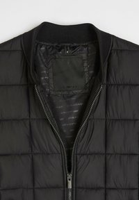 Czarna pikowana kurtka z zamkiem z przodu, prążkowanym kołnierzem i wnętrzem z logo. Posiada pikowaną fakturę i ukryty detal kieszeni.