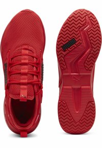 Zapatillas deportivas rojas con una parte superior de malla texturizada, cordones planos y una suela de goma moldeada que presenta un patrón de banda en zigzag y acentos de logo.