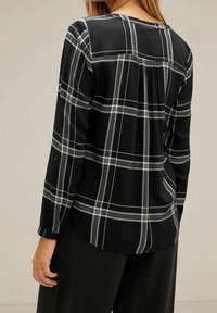 Camicia a maniche lunghe a quadri neri con righe bianche, dotata di scollatura rotonda e dettaglio di pieghe sul retro. Il tessuto sembra essere testurizzato.