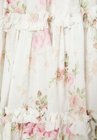 Tissu à imprimé floral doux rose et vert avec des volants froncés le long des panneaux verticaux et des coutures horizontales sur fond clair.