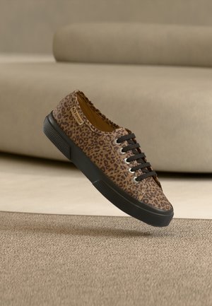 Rudos ir juodos spalvos leopardo rašto sportbačiai su juodais raišteliais ir padu, pakreipti ant smėlio spalvos kilimo su smėlio spalvos sofa fone.