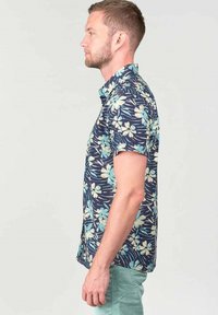 Camisa de flores de manga corta en color marino, con flores en verde claro y blanco, hecha de material de algodón, con cuello abotonado y un ajuste relajado.