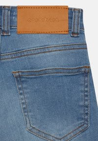 Bolsillo trasero y cintura de unos jeans de mezclilla azules con una etiqueta de cuero marrón que dice "cost:bart".