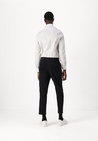 Vit skjorta med en figursydd design, matchad med mörkblå tapered-byxor och vita sneakers, sedd bakifrån.