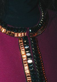 Vêtement violet foncé avec un col noir, orné de sequins décoratifs et de perles aux tons dorés et argentés le long de l'ouverture frontale.