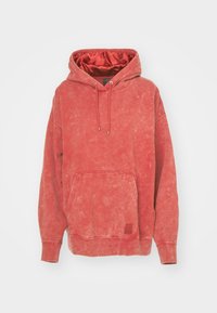 Sudadera con capucha de algodón rojo con cordón en la capucha, bolsillo frontal y acabado texturizado. Presenta puños y dobladillo acanalados con un detalle de parche de logo.