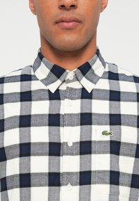 Heren overhemd met knopen in een marineblauw en grijs ruitpatroon op witte stof. Inclusief een klein groen krokodillogo op de borstzak.
