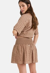 Bruine textuur cropped top met korte mouwen en een bijpassende smocked rok met een uitlopende zoom en decoratieve gaten.