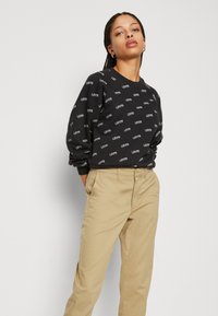 Felpa nera con motivo del logo "Levi's" bianco, collo rotondo e polsini a costine abbinata a pantaloni beige, con tasche piatte davanti e dietro.