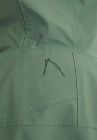 Green fabric features a smooth texture with contrasting light blue stitching. A geometric embroidered design is visible on the pocket area.