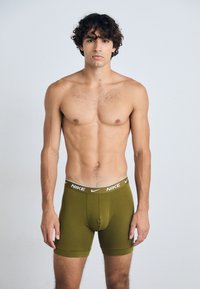 Nike men's boxer briefs in olive green, featuring a white branded waistband. The design is form-fitting with a soft texture and mid-thigh length.