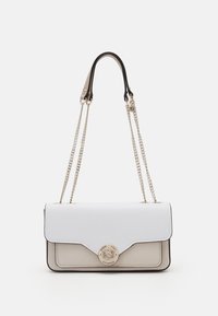 Sac à bandoulière en cuir blanc et beige avec des chaînes dorées en guise de bandoulières et un fermoir rond en métal avec le logo indiquant "Guess 1981 Los Angeles".