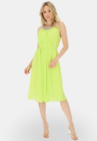 Rozszerzana sukienka do kolan w jaskrawym neonowym zielonym kolorze, z plisowanym wzorem i ozdobnym dekoltem. Zawiera pasek w talii i falbaniaste wykończenie dołu.