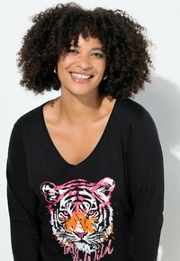 Schwarzes Langarmshirt mit V-Ausschnitt, das ein buntes Tigerdesign in Orange, Pink und Weiß zeigt, mit dem Text "Into the Wild" darunter.