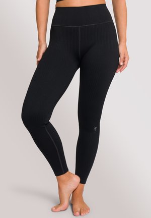 Schwarze gerippte Leggings mit hohem Taillenbund, die mit kontrastierenden Nähten und einem kleinen Logo nahe dem Knöchel versehen sind. Weiche Textur, figurbetontes Design.