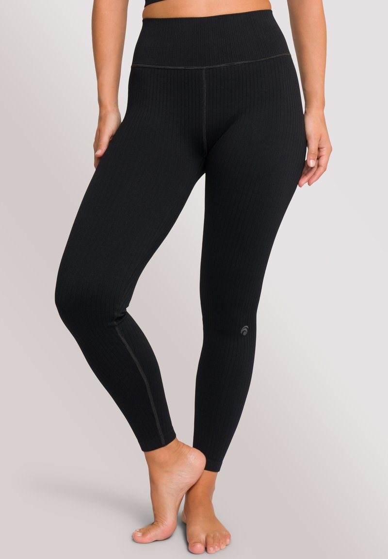 Zwarte geribbelde leggings met een hoge tailleband, voorzien van contrasterende stiksels en een klein logo nabij de enkel. Zachte textuur, aansluitend ontwerp.