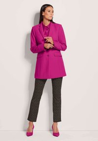 Fuchsia blazer met notch lapels en twee knopen, gecombineerd met zwarte broek met stippen en bijpassende roze hakken. Glad stof, gestructureerde pasvorm.