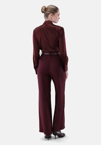 Burgundy silk blouse with long sleeves, paired with high-waisted burgundy trousers and dark heeled shoes. Smooth texture, tailored fit.