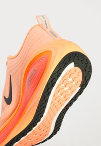 Orange und rosa Sportschuh mit schwarzem Nike-Swoosh, "ZoomX"-Dämpfungslabel und strukturiertem schwarzen und orangefarbenen Gummisohlen.