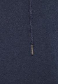 Felpa blu navy con un tessuto caratterizzato da una texture intrecciata lungo la zip e un dettaglio di tirazip metallico. Materiale liscio e flessibile.