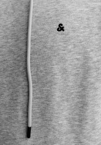Grauer Strickpullover mit einem schwarzen "&"-Logo, einer hellgrauen Kordel und dunklen Spitzen, der ein lässiges Design unterstreicht.