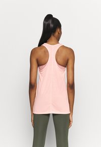 Débardeur rose clair sans manches avec larges emmanchures et dos nageur, en tissu doux. Comprend une couture verticale centrale pour la structure.
