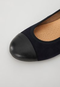 Ballet flats en daim marine avec un capot en cuir noir. L'intérieur présente une semelle intérieure brun clair avec des détails perforés.