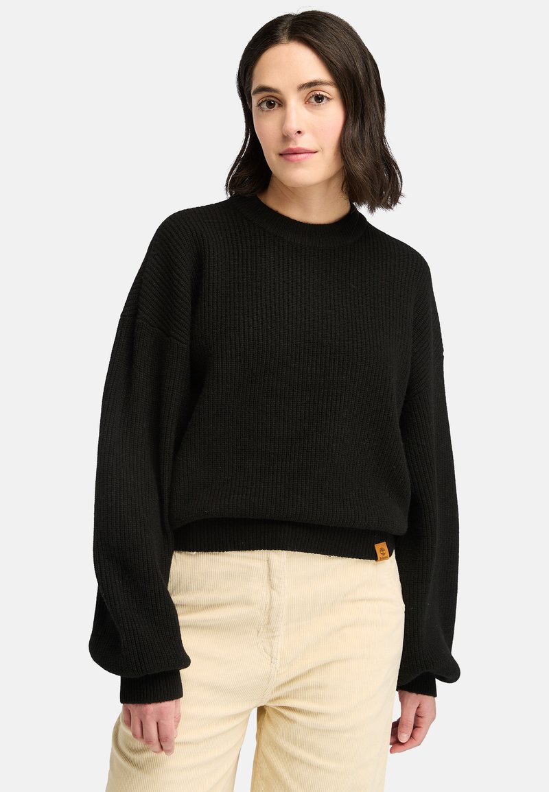 Svart ribbad stickad tröja med rund halsringning och översize ärmar, kombinerad med ljusbeige kordbyxor. Inkluderar en liten logotagg.