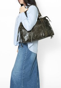 Borsa in pelle verde scuro con numerose tasche, dettagli in ottone e lunghe frange sfilacciate. La borsa ha un design strutturato e una superficie liscia.