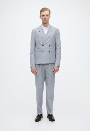 Svetlo šedý dvojradový oblekový sako s klopovými reverzami, doplnené o zodpovedajúce nohavice. Doplnky: biela košeľa, čierne topánky, prispôsobený strih.