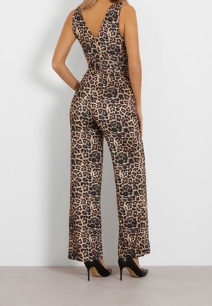 Femme portant une combinaison sans manches à imprimé léopard avec des jambes larges et des talons hauts noirs, debout de dos à la caméra.