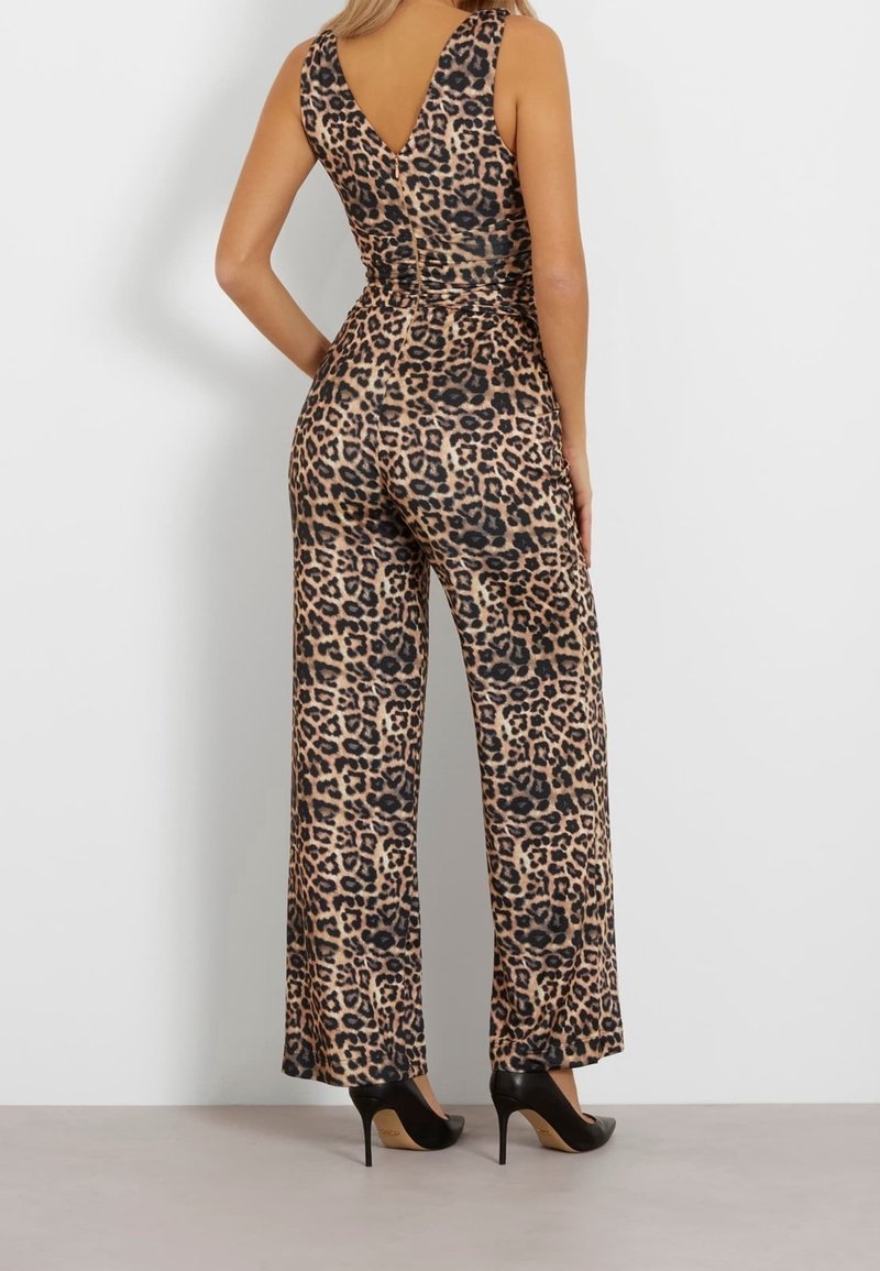 Femme portant une combinaison sans manches à imprimé léopard avec des jambes larges et des talons hauts noirs, debout de dos à la caméra.