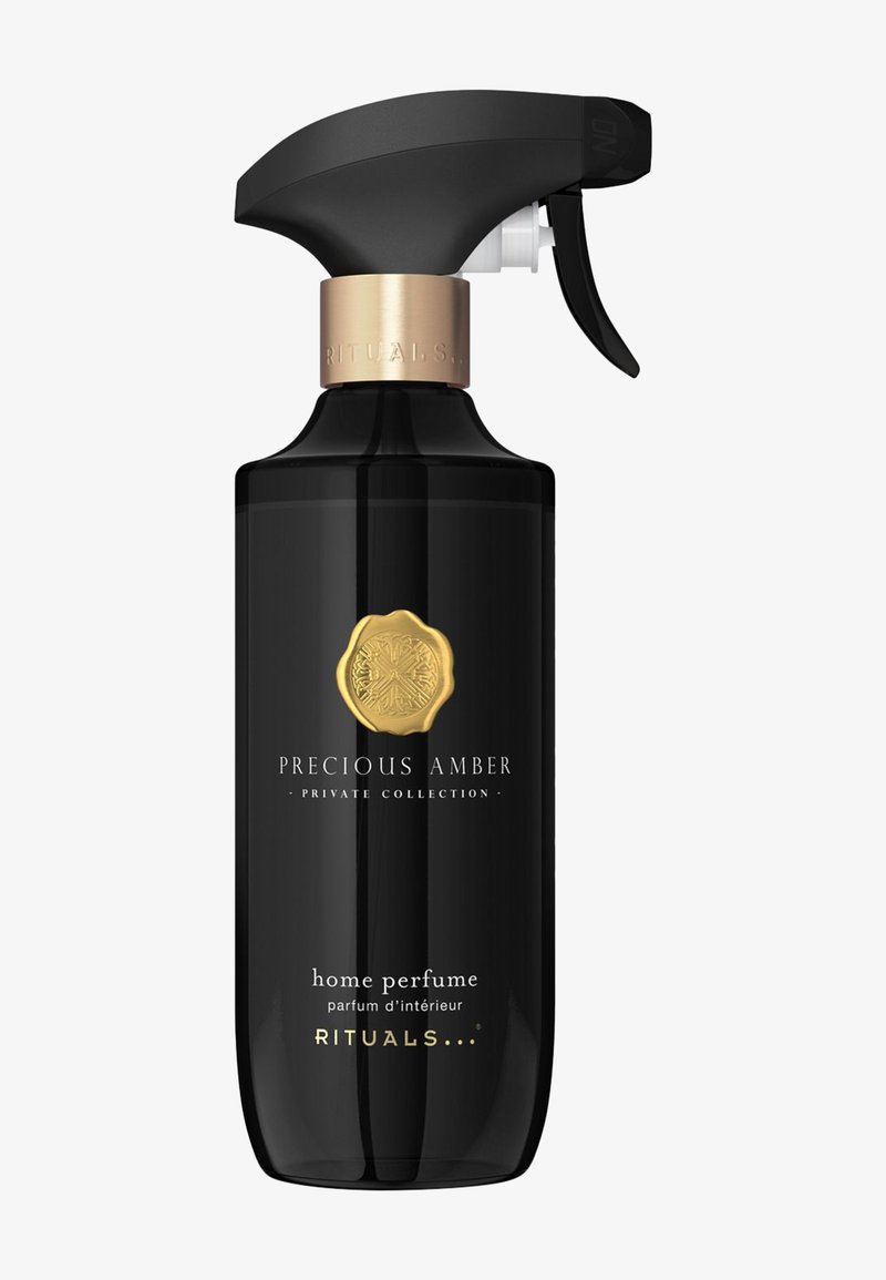 Svart sprayflaske med en gullfarget dekorasjonsring, har et rundt emblem. Etiketten viser "Precious Amber" og "home perfume" i hvit tekst.