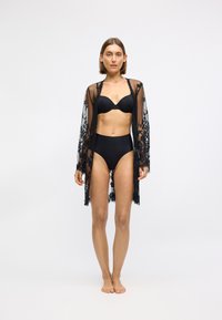 Svart blonde kimono med lange ermer, gjennomsiktig stoff, blomstermønstre, åpen front, og en avslappet passform, båret over en svart BH og høyt liv-bukser.