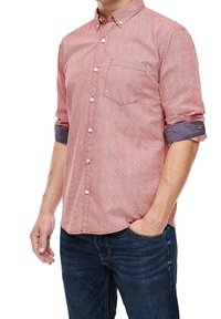 Camisa roja con un pequeño patrón blanco, cuello abotonado, un bolsillo en el pecho, mangas enrolladas, combinada con jeans azul oscura.