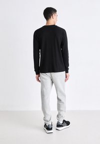 Zwarte longsleeve shirt, grijze sweatpants en zwarte sportschoenen. Het shirt heeft een ronde hals; de broek heeft elastische boorden en zakken.