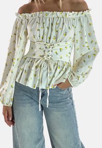 Weiße schulterfreie Bluse mit einem floralen Muster aus gelben Blumen, Ballonärmeln und einer taillierten Passform mit Schnürdetail.