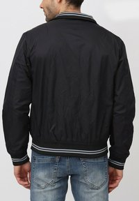 Veste bomber noire en nylon avec un col et des poignets côtelés. Elle présente une couleur unie, une texture lisse et une taille ajustée avec des rayures grises.