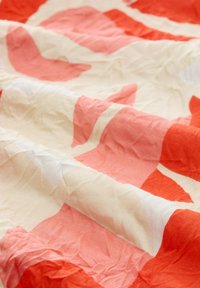 Woven cotton fabric w kolorze kremowym, z dużymi abstrakcyjnymi kształtami w kolorze koralowym i delikatnym różu, o pomarszczonej fakturze.