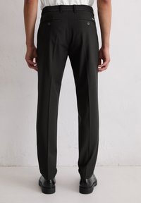 Zwarte broek met een gladde textuur, voorzien van een getailleerde pasvorm, elastische tailleband en twee achterzakken met knoopsluitingen.