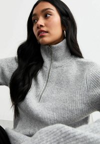 Lichtgrijze gebreide sweater met een hoge hals, voorzien van een kwart rits en een geribbelde textuur over de hele lengte.