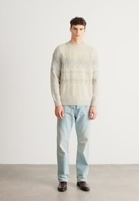 Sweter z dzianiny o fakturowanej, jasnokremowej tkaninie z geometrycznym wzorem w delikatnym niebieskim kolorze. Połączony z jasnoniebieskimi dżinsami i ciemnymi butami.