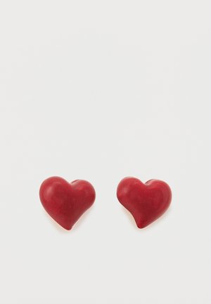 Siledad südamekujulised aksessuaarid, mis on valmistatud läikivast materjalist ja millel on sile tekstuur. Kaks südant asetsevad tihedalt üksteise lähedal valge tausta ees.