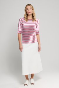 Rood-wit gestreept 3/4 mouwtopje gecombineerd met een witte midi-rok, met een rechte silhouet en soepele stof. Witte instappers maken de look compleet.