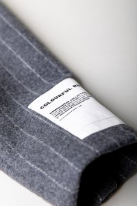 Material gri din fetru cu cusături albe și o etichetă proeminentă. Eticheta afișează numele mărcii și instrucțiunile de îngrijire cu text negru pe un fundal alb.
