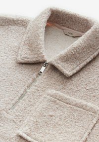 Giacca in pile con zip di colore rosa chiaro, caratterizzata da una superficie testurizzata, colletto alto e una tasca frontale. Dettagli in metallo argentato sulla zip.