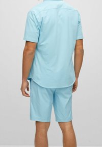 Hellblaues Kurzarmhemd mit abgerundetem Saum und passenden Shorts, gefertigt aus glattem Stoff mit lockerem Schnitt und ohne sichtbare Muster.