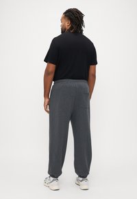 Σκούρο γκρι φόρμα με ελαστική μέση, ριμπ μανσέτες και πίσω τσέπη, σε συνδυασμό με μαύρο μπλουζάκι, από πίσω όψη.