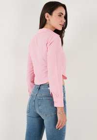 Pink cropped button-up shirt with long sleeves, paired with high-waisted blue jeans. Features a tailored collar and cuff detail.