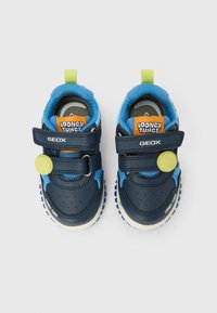 Marineblå og blå barne-sneakers med borrelåsstropper, grønne tennisballdekorasjoner og "Looney Tunes"-merke på tungen og tærne.